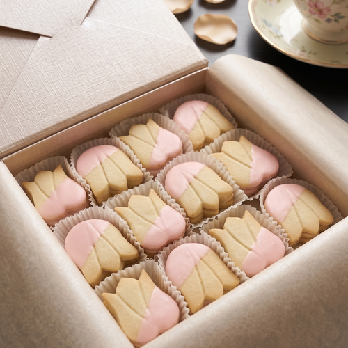 Box of 36 pink-tined shortbread cookies with a cup of tea on a saucer.
