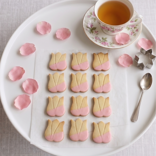 Decorative shortbread cookies shaped like tulips on a plate with a cup of tea.
