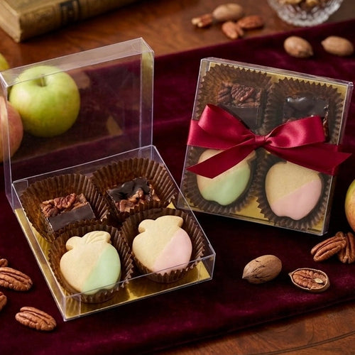 Two gift boxes with pastries and a red ribbon on a wooden surface with apples and nuts.
